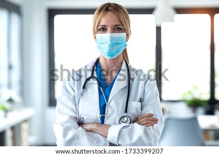 Portrait of young female doctor in medical mask looking at camera in the consultation.