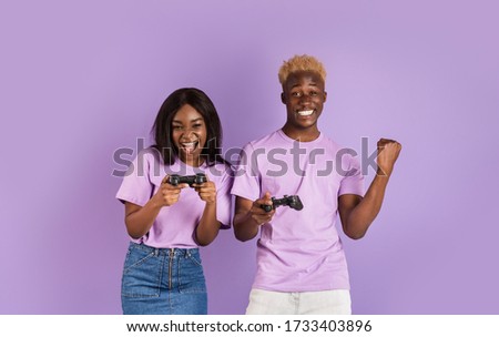 Fun hobbies concept. Cool black guy playing video games with his girlfriend on lilac background. Panorama