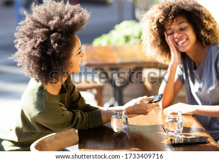 Portrait two happy young african american women sitting at outdoor cafe with mobile phone
