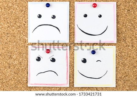 Different emotions, hand-drawn, on square sheets of paper pinned to a cork board