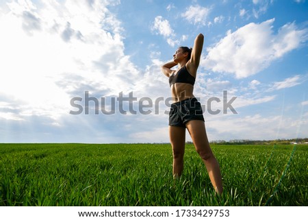 Girl athlete does warm-up outdoors, exercises for muscles. Young woman go in for sports, healthy lifestyle, athletic body. She is in sportswear, black top and shorts. Sport concept.
