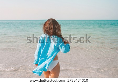 Young beautiful woman relaxing on the beach. Back view of happy girl in blue shirt and swimsuit