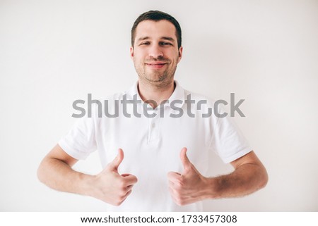Young man isolated over white background. Positive cheerful attractive guy holding two big thumbs up and smile. Posing alone on camera.