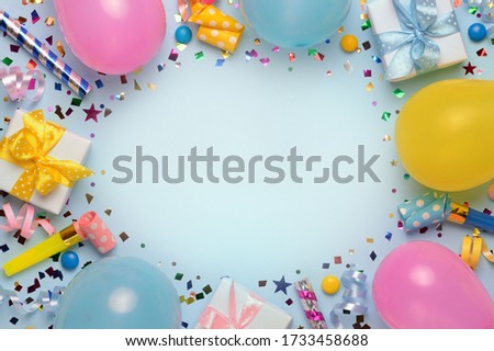 Holiday frame or background with colorful balloon, gift, confetti, silver star, carnival cap and streamer. Birthday or party greeting card with copy space. Flat lay, top view. 