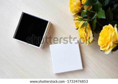Top view for presentation. An empty jewelry box, a gift with a black velvet bottom. Place for a logo, text sale. Bouquet of yellow roses on a light wooden table. Royalty-Free Stock Photo #1733476853