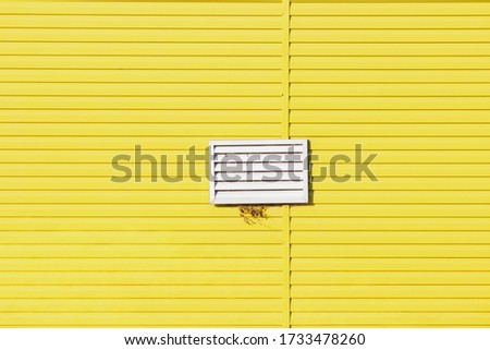 Yellow background made of plastic panels and a white plastic grille on it.