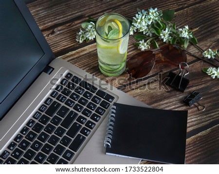 laptop, notepad and glass of refreshing cocktail on a wooden background. concept of remote work or outdoor work. Out of office work concept horizontal