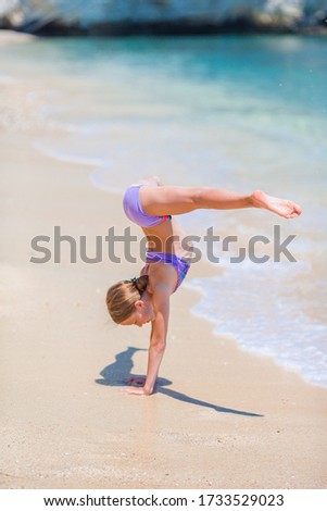 Little girl having fun at tropical beach during summer vacation playing at shallow water. Cute kid making sporty exercises on the seashore