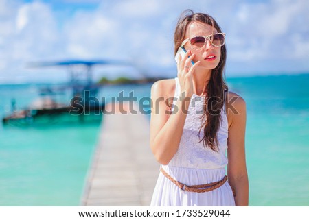 Young happy woman on white beach talking by smartphone. Young beautiful woman having fun on tropical seashore.