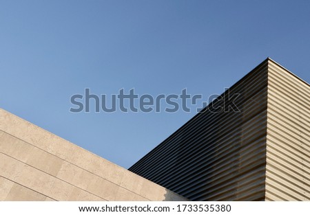 Triangle side corner of wide minimal building backlit by sun in suburban district. Minimal urban details, simple geometric lines against sky.