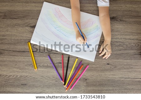 Photos from above for colorful rainbow drawing by color pencils on white paper placed on a wooden table by preschoolers which will see two arms for learning to develop creativity and enjoyment.