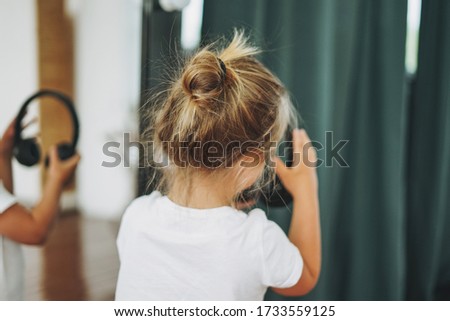 Little toddler girl with fair hair with headphones from behind having fun in studio