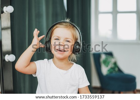 Cute happy toddler girl with fair hair in headphones having fun in bright interior