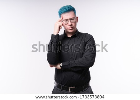 Young blue haired man touching his temple with fingers, expressing serious decision making, studio shooting on light background
