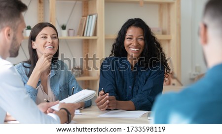 Happy african american businesswoman telling employees about project sit at table in coworking boardroom at meeting. Smiling laughing diverse female leader discuss business strategy colleagues. Royalty-Free Stock Photo #1733598119