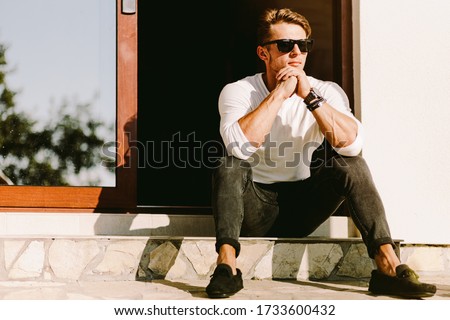 portrait of a brutal handsome man in sunglasses and watch outdoors at home. Stylish man wearing casual. Men's beauty, fashion. Optics for men. Royalty-Free Stock Photo #1733600432