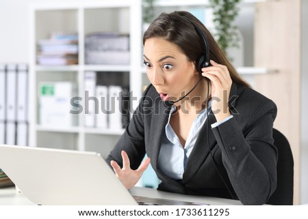 Surprised telemarketer woman with headset reading good news on laptop sitting on a desk at office Royalty-Free Stock Photo #1733611295