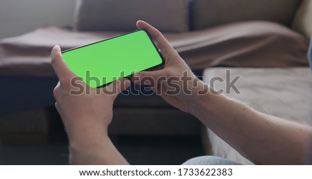 Closeup young man sit on a couch and watch something on a smartphone with green screen