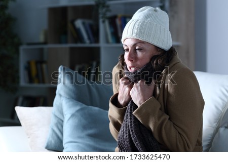 Cold adult woman covered with clothes freezing sitting on the sofa at night at home Royalty-Free Stock Photo #1733625470