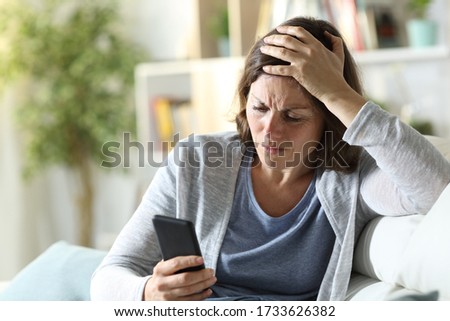 Sad adult woman reading bad news on smart phone sitting on a couch at home Royalty-Free Stock Photo #1733626382