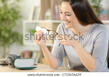 Happy woman cleaning eyeglasses with tissue paper sitting on a desk at home Royalty-Free Stock Photo #1733636639
