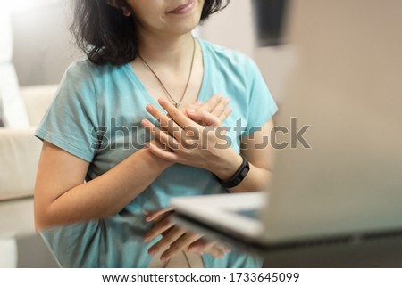 Young woman in blue shirt with sincere smile showing grateful gesture with touching on her chest with hands. Asian girl feeling thankful people with using laptop computer and internet technology.


