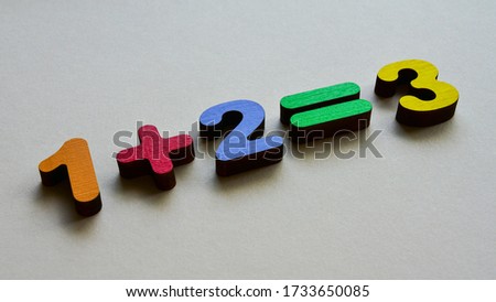 Wooden multi-colored numbers 
illustrate the addition function on a beige background. Side view. Elementary mathematics, Children's day. 
