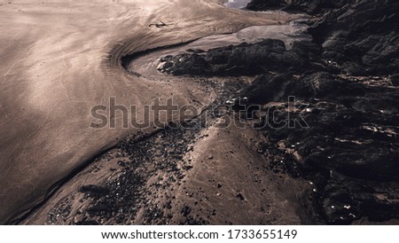Close up picture of s shape trench curved by flowing water in sand around rocks on the beach.Light and shadows.Nature abstract.