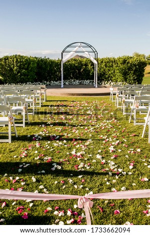wedding ceremony aisle with chairs and flower petals leading to arch