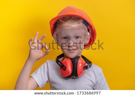 Handsome boy in builder glasses, helmet and headphone to ear protection shown ok sign over yellow background copy space