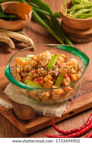 Sambal goreng kentang is served in a bowl on a wooden table. is a traditional Indonesian food, made from fried potatoes mixed with spicy seasonings and peas. special dishes served during Eid