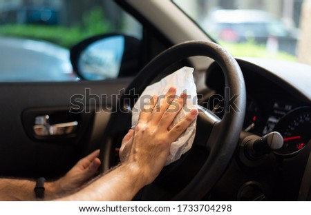 Man cleaning his car steering wheel for disinfection and a safe ride during the virus pandemic closeup Royalty-Free Stock Photo #1733704298