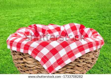 Empty picnic basket. Close-up of a empty straw basket therein a red checkered napkin isolated on a green grass background. For your food and product display montage. Macro.