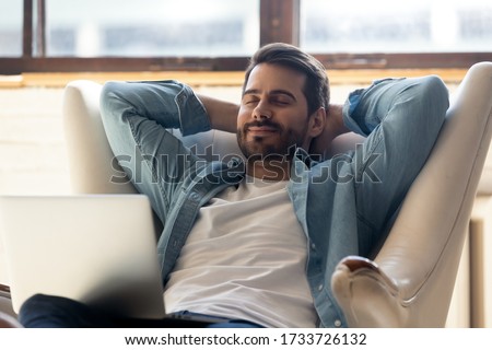 Smiling young man relax in comfortable armchair at home take nap daydream distracted from computer work, happy millennial male sit rest in cozy chair in living room enjoy peace, stress free concept Royalty-Free Stock Photo #1733726132