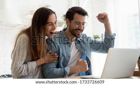 Overjoyed millennial couple sit at desk look at laptop screen feel euphoric with online win, excited happy young husband and wife read good news, get unexpected notification on computer, luck concept Royalty-Free Stock Photo #1733726609