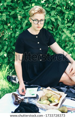 Pretty young woman drawing with watercolor outdoors sitting on green grass in a beautiful place in the rays of the sun. Picnic ideas