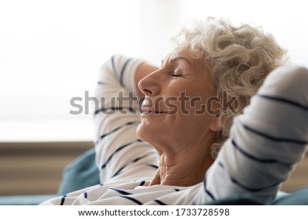 Side close up head shot view tranquil calm middle aged hoary woman crossed hands behind head, relaxing on cozy sofa alone. Peaceful mindful mature senior grandmother daydreaming meditating at home. Royalty-Free Stock Photo #1733728598