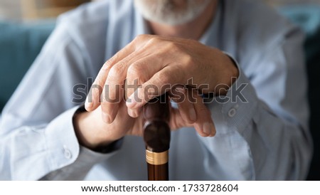 Close up elderly mature middle aged disabled man leaning wrinkled hands on walking cane. Retired elderly grandfather using wooden stick. retirement healthcare arthritis disability problem concept. Royalty-Free Stock Photo #1733728604