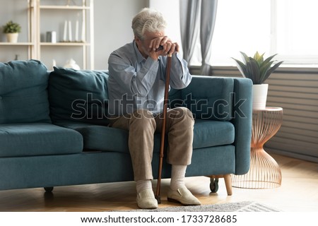 Full length exhausted disabled middle aged old man resting on sofa, leaning on walking cane, suffering from depression alone at home. Upset hoary elder senior grandfather tired of hard rehabilitation. Royalty-Free Stock Photo #1733728685