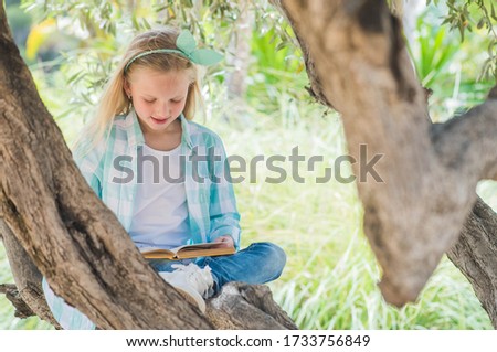 Blonde girl reading a book on a large spreading tree.