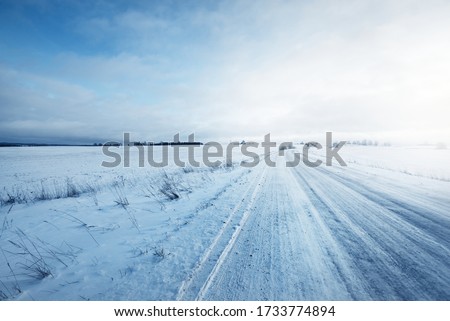 Snow-covered country road through the fields after a blizzard at sunset. Old rustic house in the background. Winter rural scene. Dramatic sky, colorful cloudscape. Ice desert. Lapland, Finland Royalty-Free Stock Photo #1733774894