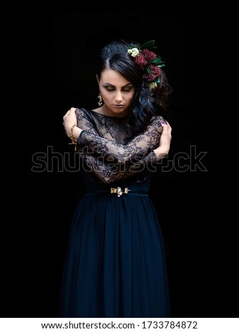 A woman in a black dress with makeup and flowers in her hair on a black background. Gothic style