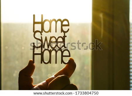 yellow wooden letters with word - HOME SWEET HOME - IN MALE HAND. lettering on sunny window background.
