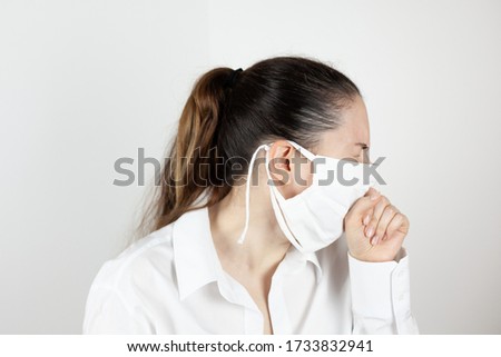 A young girl in a mask coughs and covers her face with her hand out of habit. Demonstration of habits. Life during the pandemic. The first signs of the disease.