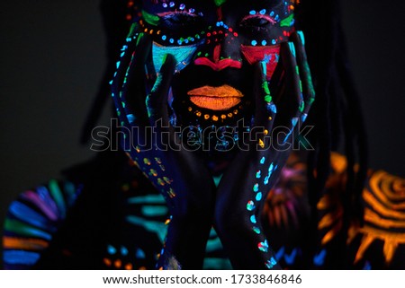 Conceptual portrait of young african man painted in glowing fluorescent UV colors, man touch his face, with eyes closed. make-up, body art concept, isolated studio shoot