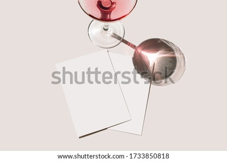 Summer stationery still life scene. Glass of red wine, cocktail, long shadow. Blank greeting cards mockups scene. Pink table background in sunlight. Flat lay, top view. Birthday, celebration, concept
