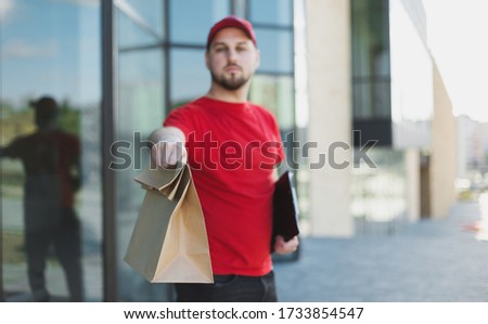 Young handsome deliveryman in red uniform with brown paper package