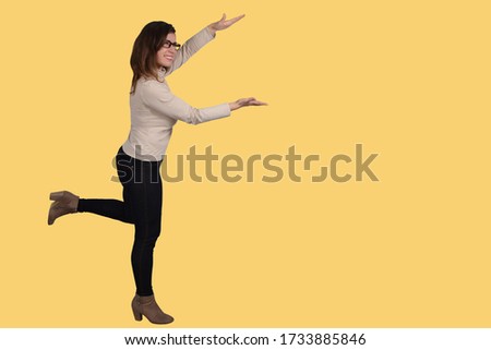 A girl in full growth, in profile, in a running pose with her arms extended forward, presents, laughs, on a yellow background.Advertisement concept. Offering banner with women