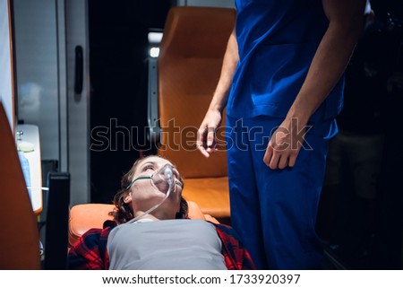 A woman lying on a stretcher with an oxigen mask on and looking at the paramedic in a blue uniform Royalty-Free Stock Photo #1733920397