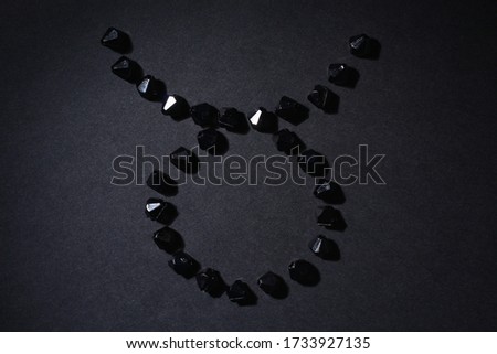 Symbol of the zodiac sign Taurus made by black stones on a black background. Low dark key. Vignetting lighting. Horoscope Theme